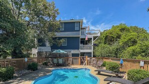 A swimming pool with a wooden deck and lounge chairs, surrounded by a wooden fence and trees. - Windance - 5 BR Vacation Home on Private Lot w/Pool, Hot Tub, Dogs Allowed (Southern Shores)