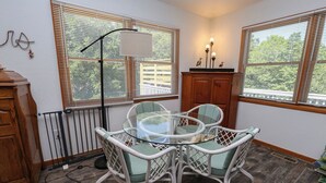 A dining area with a glass table and white wicker chairs, wooden cabinets, and a view through large windows. - Windance - 5 BR Vacation Home on Private Lot w/Pool, Hot Tub, Dogs Allowed (Southern Shores)