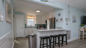A modern kitchen with white cabinets, a stainless steel refrigerator, and a bar area with stools. - Sandy Pointe -  4 BR Oceanside Home in Duck w/Private Pool, Hot Tub, Dogs Allowed (Duck)