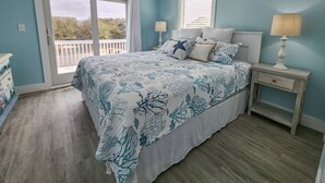 A bedroom with a bed, two bedside tables, a ceiling fan, and a view through a sliding glass door. - Sandy Pointe -  4 BR Oceanside Home in Duck w/Private Pool, Hot Tub, Dogs Allowed (Duck)