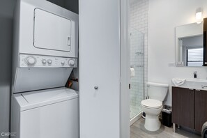 Enjoy a refreshing shower in this bathroom featuring a glass enclosure, washer and dryer, and a convenient vanity with mirror.