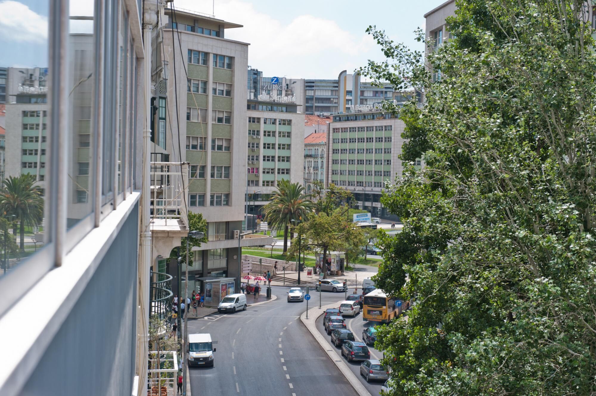 A street view with modern buildings, parked cars, and a bus.