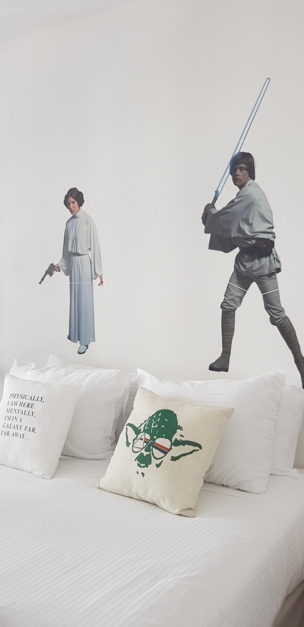 A bedroom with a bed, pillows, and two wall decorations of characters from Star Wars.