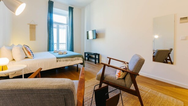 Et hotelværelse med seng, skrivebord, stol, fjernsyn og et vindue med gardiner.
