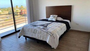 Une chambre dotée d’un grand lit, d’une tête de lit en bois et offrant une vue sur l’extérieur grâce à une porte-fenêtre coulissante.