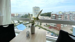 A room with a view of a cityscape, a table with a vase of flowers, and a chair.