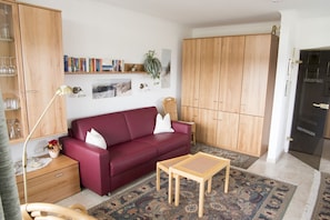 A living room with a red sofa, wooden cabinets, a small table, and a patterned rug.