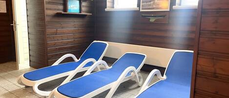 A room with four blue lounge chairs, wooden panel walls, a small shelf with a framed picture, and a door labeled "FOURTH".