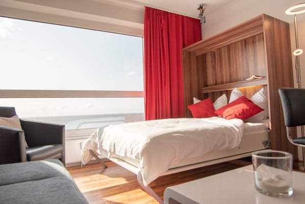 Een moderne hotelkamer met een groot bed, rode gordijnen, een houten hoofdbord, een bureau en een stoel.