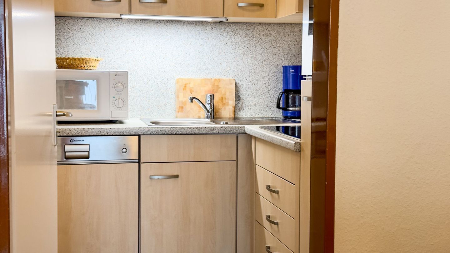 Une cuisine compacte équipée d’un four à micro-ondes, d’une machine à café et d’une planche à découper en bois.