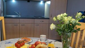 A breakfast setup with a table, a vase of flowers, and a kitchen area in the background. - FB 03.04 - Strandnahe Gemütliche 2-zimmer Ferienwohnung - Frische Brise (Cuxhaven)