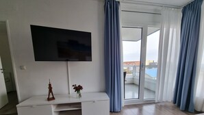 A modern living room with a flat-screen TV mounted on the wall, a white entertainment unit, and a view of the outside through large glass doors. - Frische Brise, September 2—Newly Renovated Vacation Rental - Haus Frische Brise (Cuxhaven)