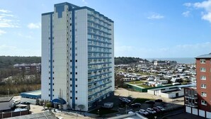 A tall, modern hotel with a flat roof and multiple floors. It is surrounded by a parking lot with several cars and a nearby RV park. - Frische Brise, September 2—Newly Renovated Vacation Rental - Haus Frische Brise (Cuxhaven)