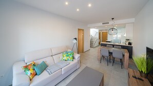 A modern living room with a sofa, a coffee table, and a dining area with chairs and a table. - Apartamento El Nido - Mar de Pulpi (San Juan de los terreros)