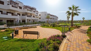 A modern residential complex with multiple balconies, a paved walkway, and a palm tree. - Apartamento El Nido - Mar de Pulpi (San Juan de los terreros)