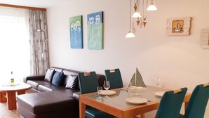 Un salon moderne avec un canapé, une table à manger dressée pour deux personnes et des œuvres d’art accrochées aux murs.