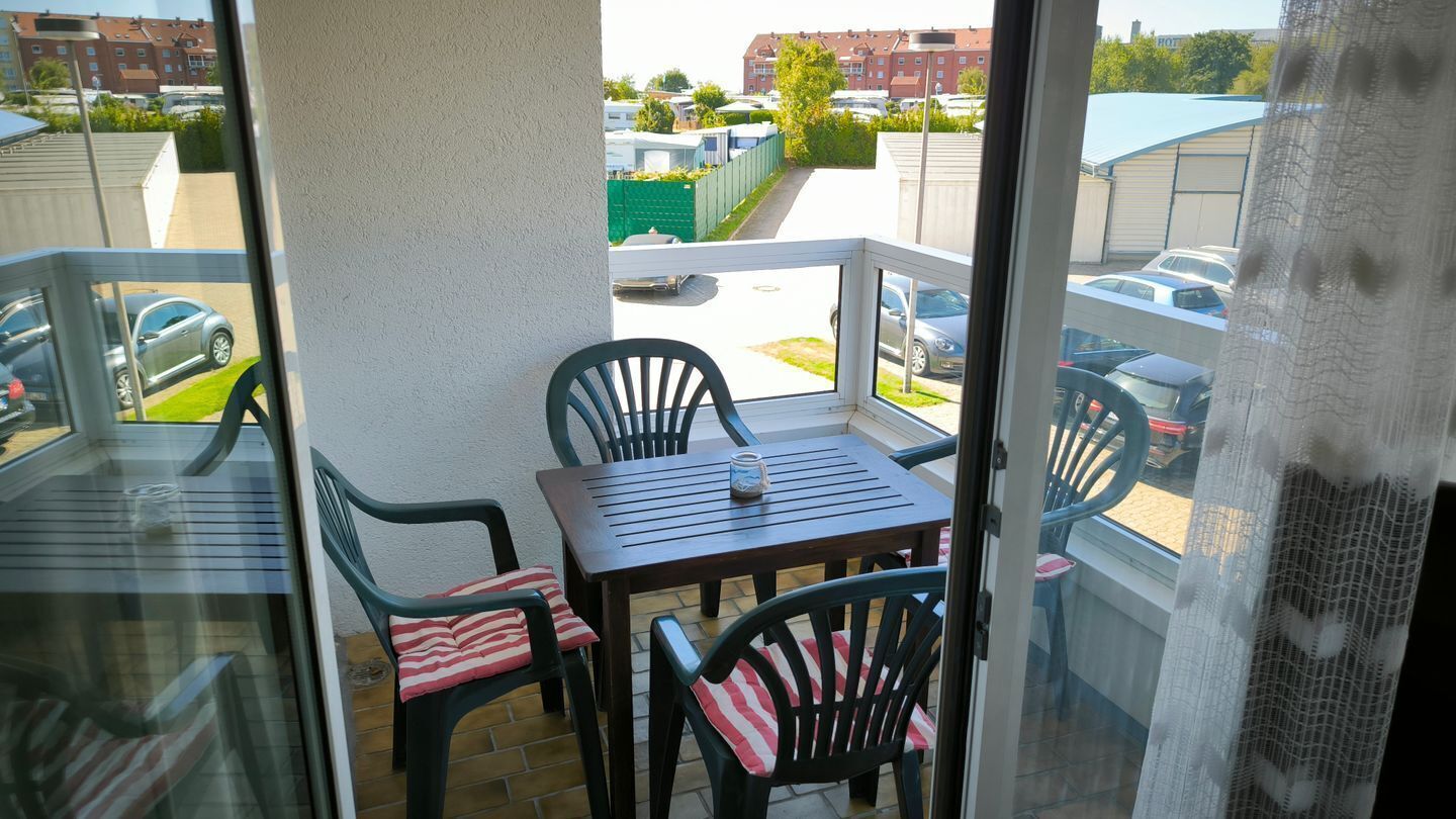A balcony with a table and chairs, a glass door, and a view of parked cars and buildings.