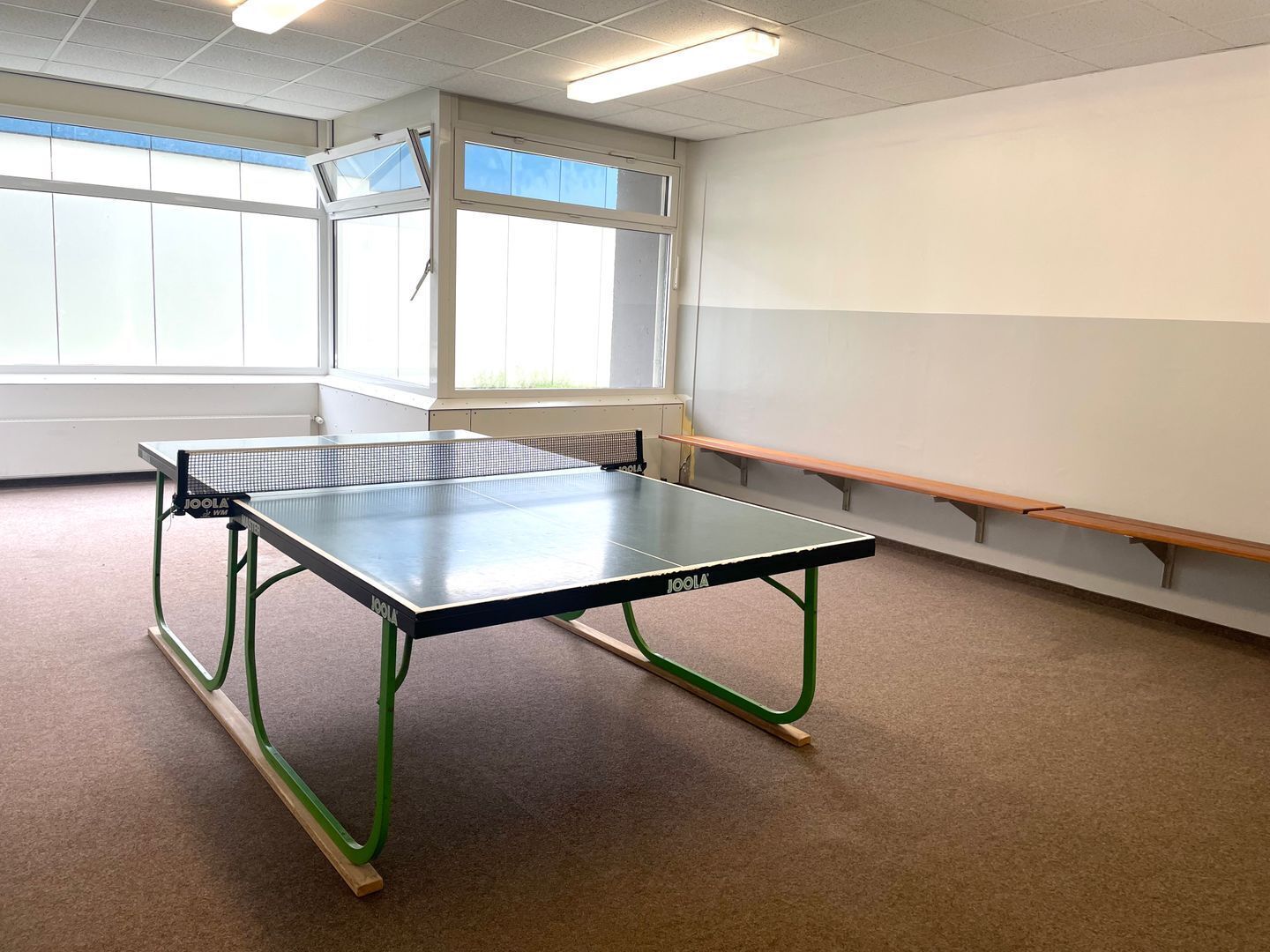 Une pièce avec une table de ping-pong, des bancs et une grande fenêtre.