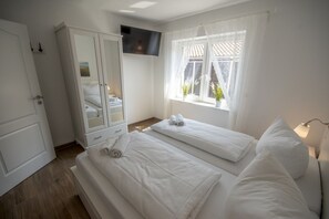 Habitación de hotel con dos camas, un armario, televisor montado en la pared y una ventana con cortinas.