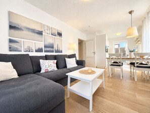 A modern living room with a grey sofa, white coffee table, and a dining area with white chairs and a table. - DS2 - Nordic-style vacation rental near the beach for 4 people - House (Cuxhaven)