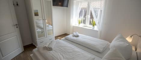 A hotel room with two beds, a wardrobe, a TV mounted on the wall, and a window with curtains.