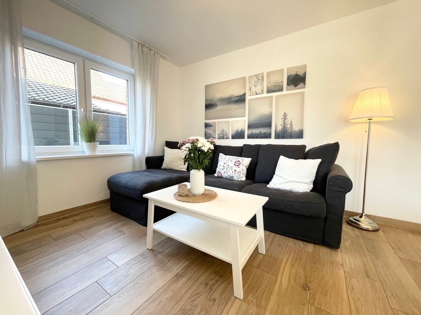 Ein modernes Wohnzimmer mit einem dunkelgrauen Sofa, einem weißen Couchtisch und einer Stehlampe.