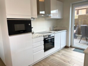 Cocina compacta con muebles blancos, un microondas Bosch, horno integrado y un lavamanos.
