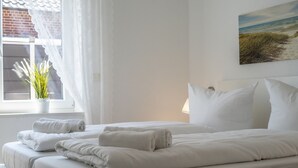 A hotel room with a bed, pillows, a window with curtains, a plant, and a painting on the wall. - DS2 - Nordic-style vacation rental near the beach for up to 4 people - House (Cuxhaven)