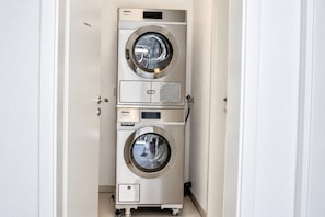 A compact, stainless steel, three-tiered, professional-grade, front-loading washing machine in a narrow hallway. - DS2 - Nordic-style vacation rental near the beach for 4 people - House (Cuxhaven)