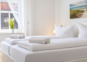 A hotel room with two beds, white linens, a potted plant, and a painting of a beach. - DS2 - Nordic-style vacation rental near the beach for 4 people - House (Cuxhaven)