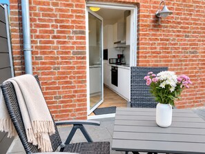 A patio area with a table and chairs, a vase of flowers, and a view into a kitchen through an open door. - DS2 - Nordic-style vacation rental near the beach for 4 people - House (Cuxhaven)
