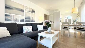 Een moderne woonkamer met een modulaire bank, een witte salontafel en een eethoek met witte stoelen.