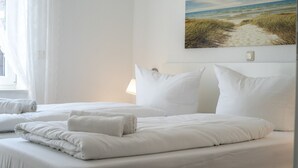 A hotel room with a bed, pillows, a painting of a beach, and a window with curtains.