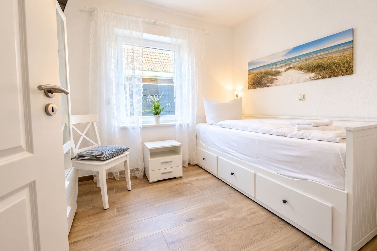 Une chambre à coucher avec un lit, une chaise, une petite table et une fenêtre avec des rideaux.