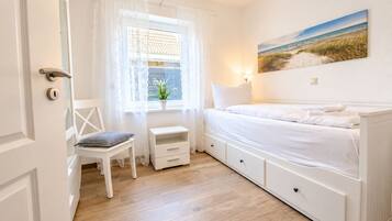 Une chambre à coucher avec un lit, une chaise, une petite table et une fenêtre avec des rideaux.