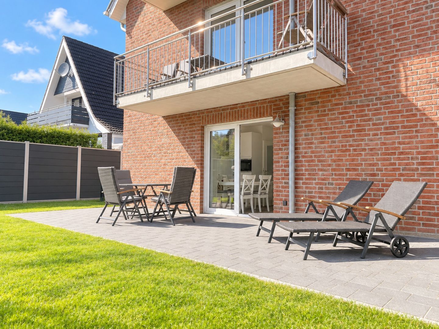 Un immeuble résidentiel à la façade en briques, doté d’un balcon avec une rambarde en métal et d’un patio aménagé avec du mobilier d’extérieur.
