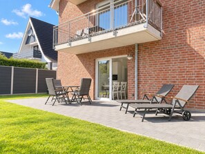 Un edificio residencial con fachada de ladrillo, un balcón con barandilla metálica y un patio con mobiliario exterior.