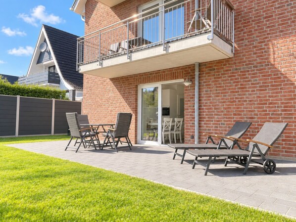 Un edificio residencial con fachada de ladrillo, un balcón con barandilla metálica y un patio con mobiliario exterior.