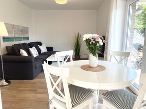A modern living room with a round white table, white chairs, a black sofa, and a vase of flowers.