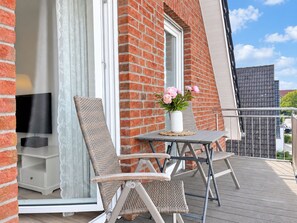 A balcony with wicker furniture, a white vase with flowers, and a TV on a stand.