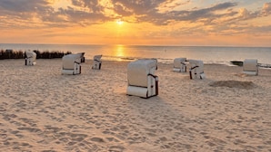 Una playa con sillones de descanso dispuestos para tomar el sol, cielo despejado y el océano al fondo.