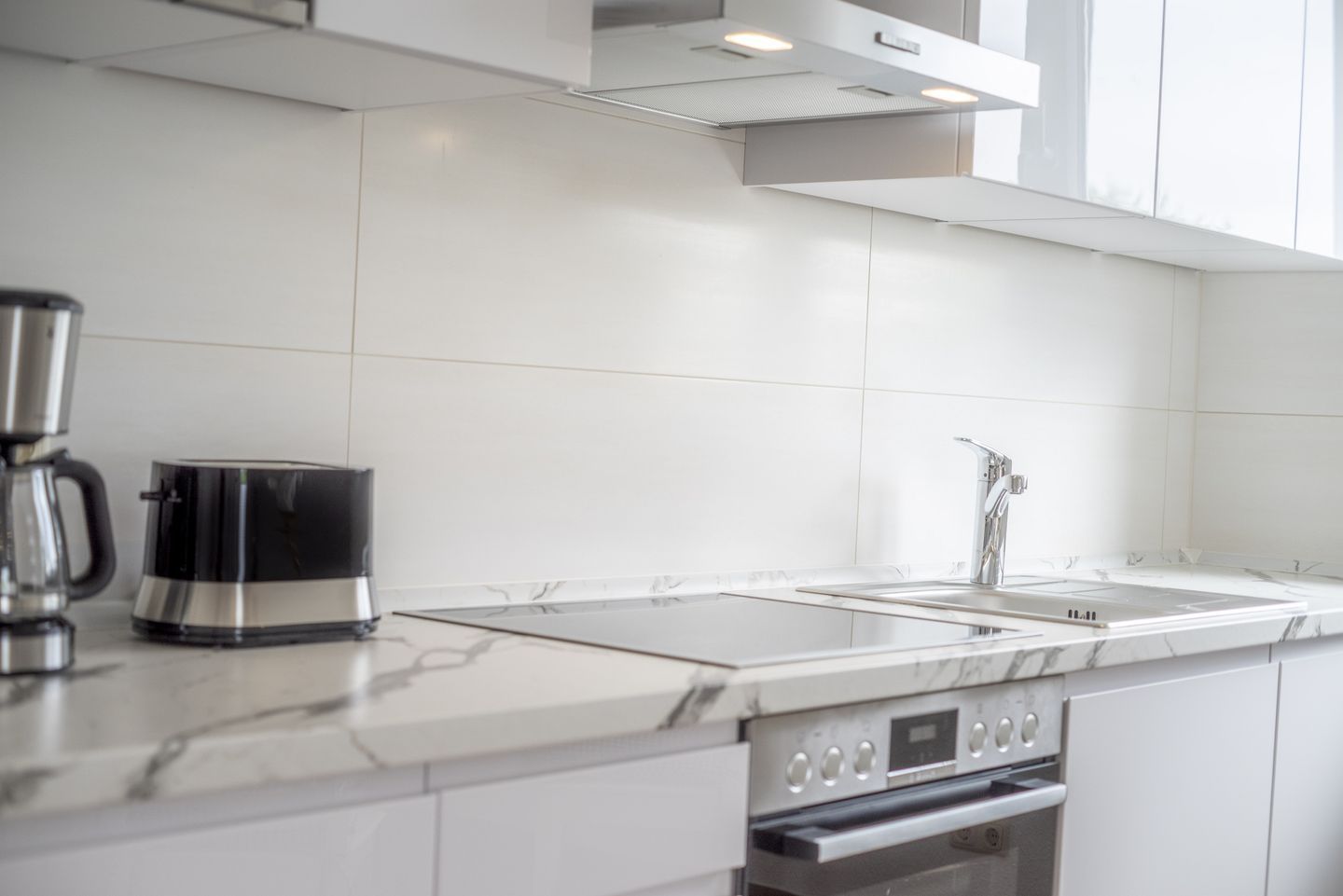 Eine moderne Küche mit weißen Fliesen, einer Edelstahl-Kaffeemaschine, einem Spülbecken und einem Backofen.