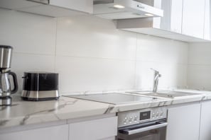 Una cocina moderna con baldosas blancas, una cafetera de acero inoxidable, un lavabo y un horno.