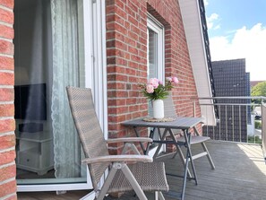 A balcony with wicker chairs, a small table, and a vase of flowers.