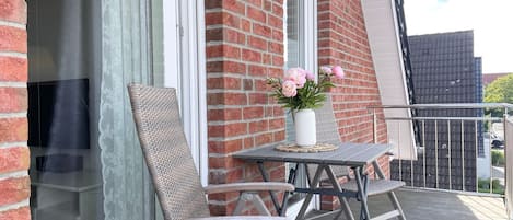En balkong med flätade stolar, ett litet bord och en vas med blommor.