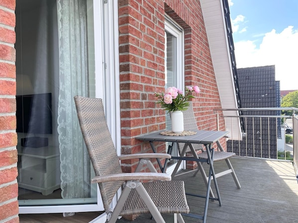 Un balcón con sillones de mimbre, una mesita y un florero.