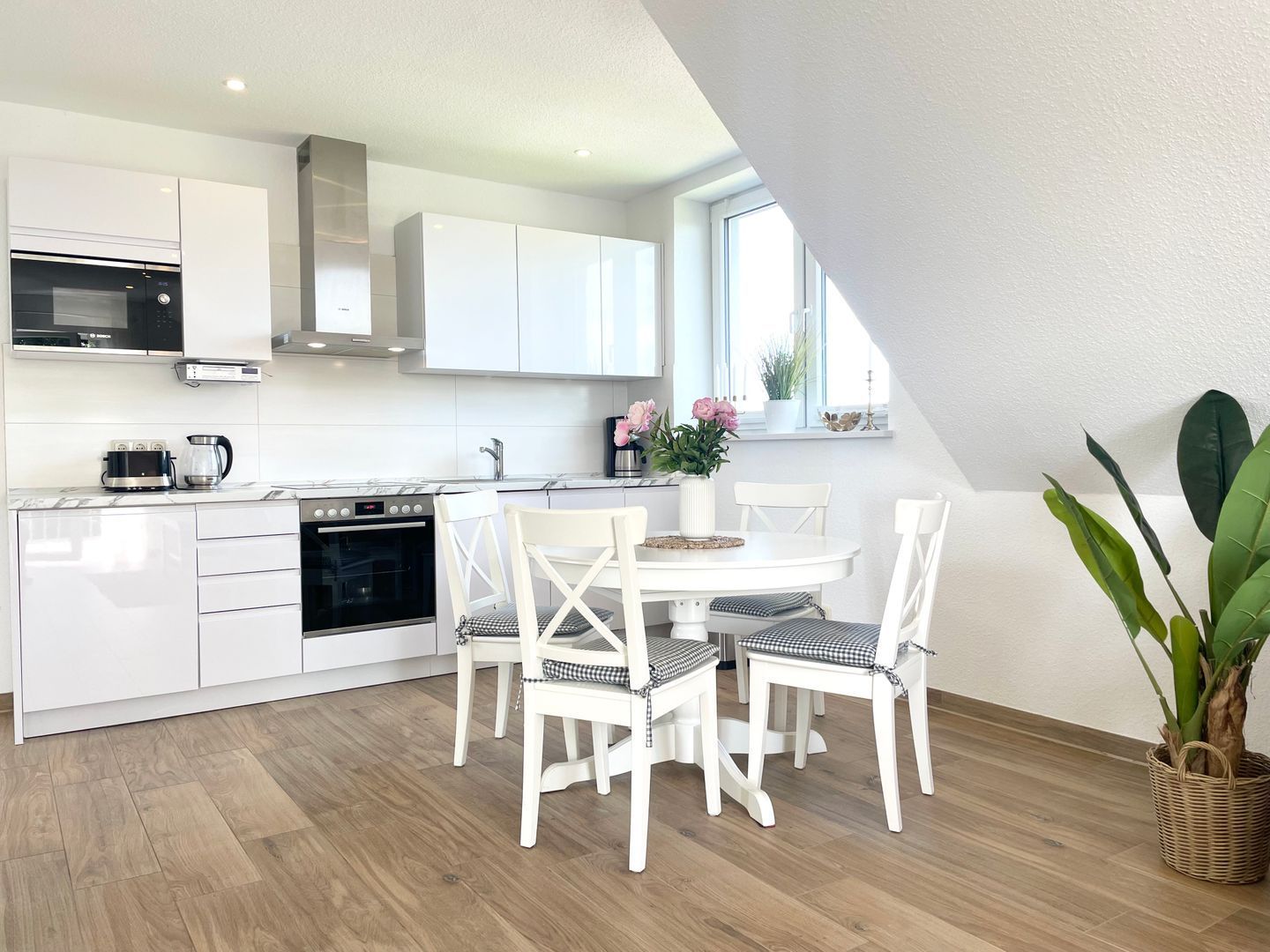 Eine moderne Küche mit weißen Schränken, einem eingebauten Backofen und einem Essbereich mit weißen Stühlen und einem Tisch.