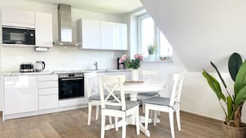 Eine moderne Küche mit weißen Schränken, einem eingebauten Backofen und einem Essbereich mit weißen Stühlen und einem Tisch.