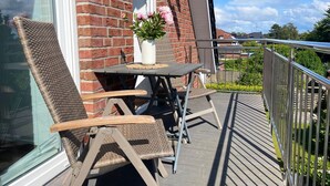 Ein Balkon mit Korbstühlen, einem Tisch mit Blumenvase und einer Backsteinmauer.