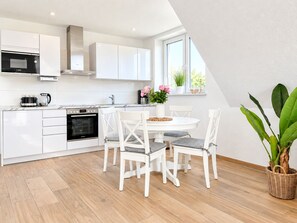 A modern kitchen with white cabinetry, a built-in oven, and a dining area with white chairs and a round table.